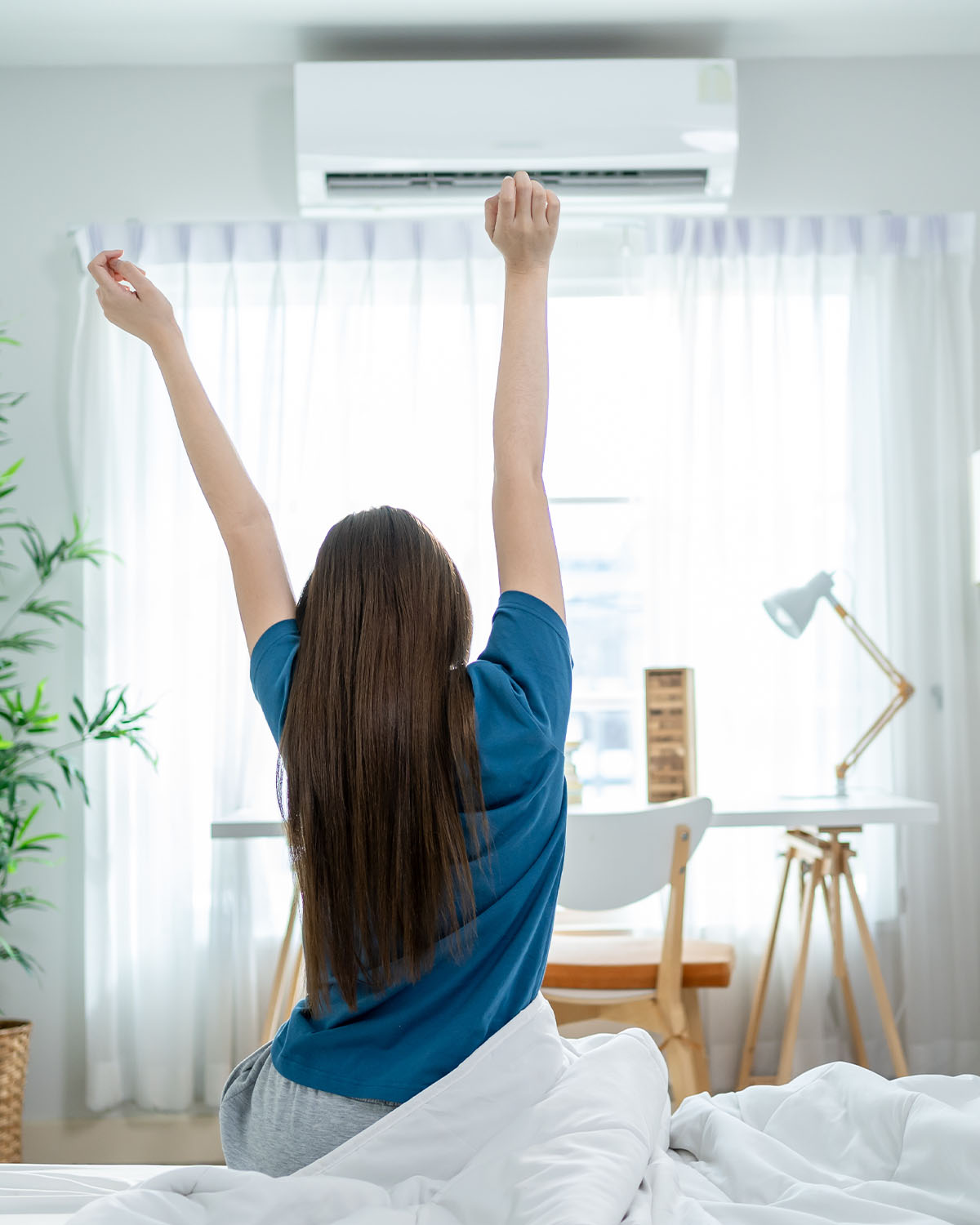 Frau streckt sich morgens im Bett unter Klimaanlage — erholt aufwachen mit kühlem Raumklima
